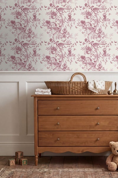 Kinderzimmer mit Tapete mit Vogel- und Blumenmuster über Wandvertäfelung und einer Holzkommode mit Weidenkorb.