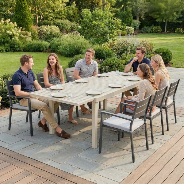 Sechs Personen sitzen an einem großen rechteckigen Gartentisch mit modernen Gartenstühlen auf einer Terrasse in einem hellen grünen Garten.