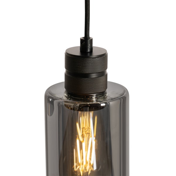 Pendelleuchte mit rauchgrauem Glaszylinder, schwarzer Metallfassung mit Rändelung und LED-Filament-Leuchtmittel.