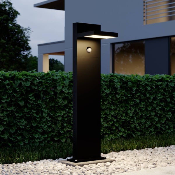 Moderne schwarze LED-Wegelampe mit Bewegungsmelder vor einer Hecke im Garten.