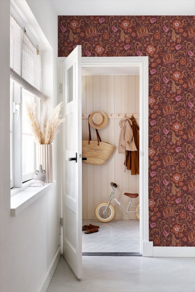 Zimmer mit floraler Mustertapete, Tür und Blick in einen Flur mit Holzvertäfelung und Laufrad.