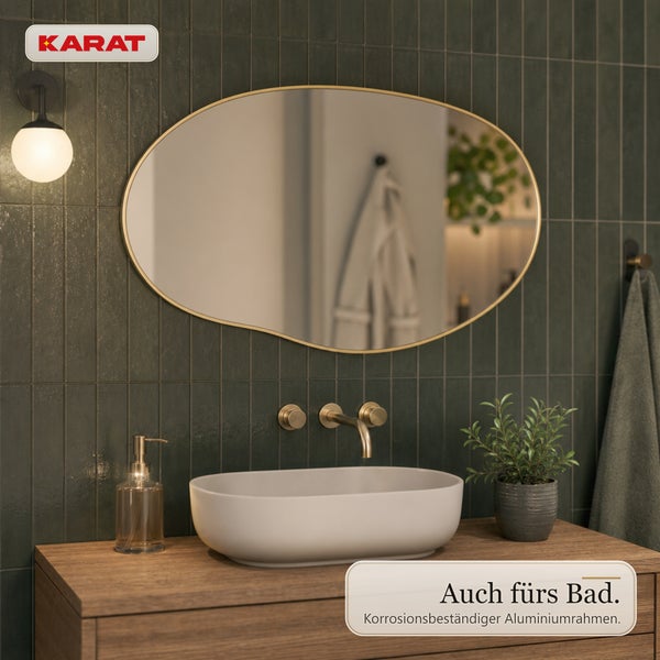 Ovaler Wandspiegel mit Aluminiumrahmen über einem Waschbecken in einem Badezimmer mit dunklen Fliesen und Holztischplatte, Karat Logo.