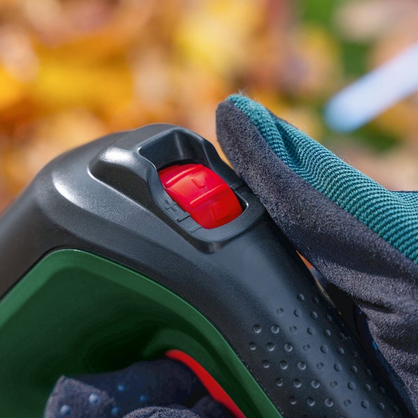 Nahaufnahme des Ein- und Ausschalters einer Gartenmaschine, bedient mit einem behandschuhten Finger.