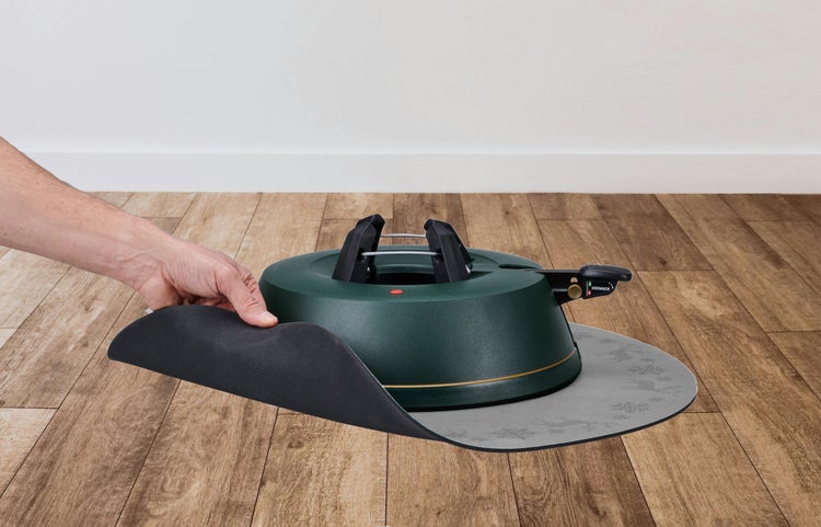 Krinner Christbaumständer auf einer runden Bodenschutzmatte mit Rentier- und Schneeflockenmuster auf einem Holzfußboden.