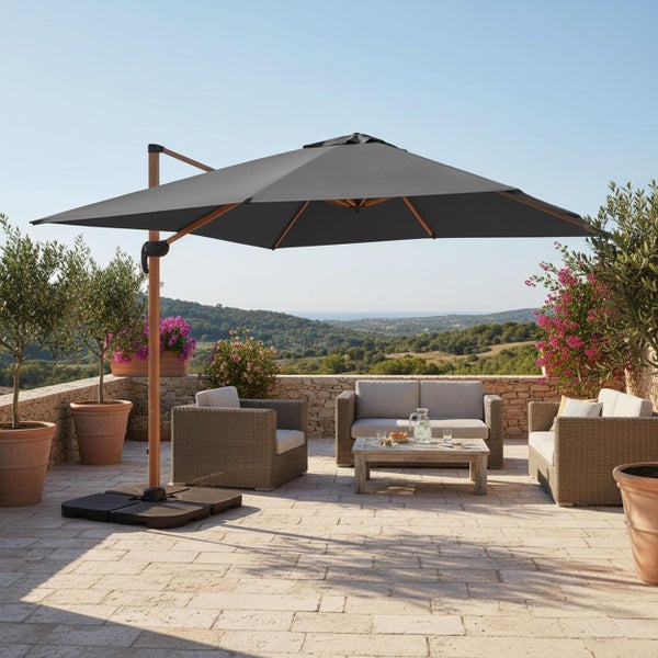 Ampelschirm in Anthrazit mit Mast in Holzoptik auf einer Steinterrasse mit Gartenmöbeln aus Geflecht und Blick auf eine Hügellandschaft.
