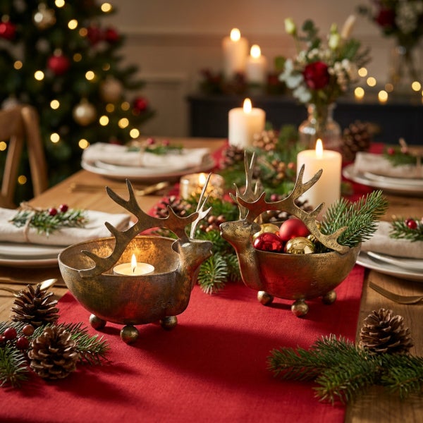 Zwei hirschfoermige Metallschalen als Weihnachtsdekoration auf einem festlich gedeckten Tisch mit Kerzen Tannenzweigen und Weihnachtskugeln