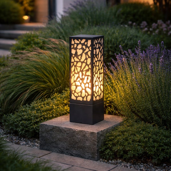 Rechteckige Außenstehleuchte mit dekorativem Lochmuster auf einem Steinsockel in einem Garten mit Lavendel und Gräsern.