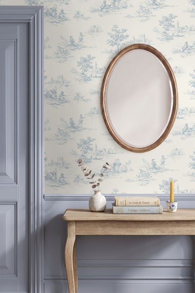 Klassische Inneneinrichtung mit Toile-de-Jouy-Tapete, ovalem Spiegel und einem hölzernen Konsolentisch vor einer blaugrauen Wandtäfelung.