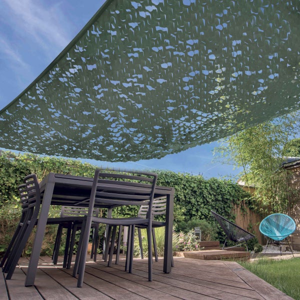 Sonnensegel in Camouflage-Optik über einer Gartenterrasse mit Esstisch und Stühlen vor einer Hecke.