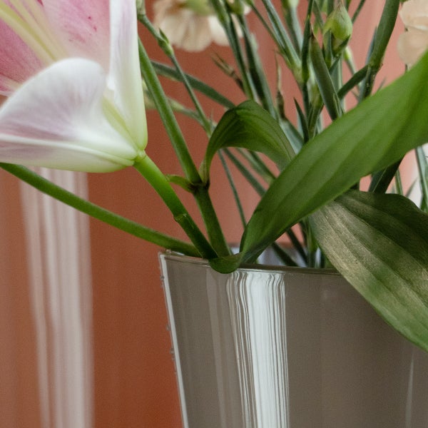 Blumenvase mit einer Lilie und grünen Blättern in einer glänzenden grauen Vase.