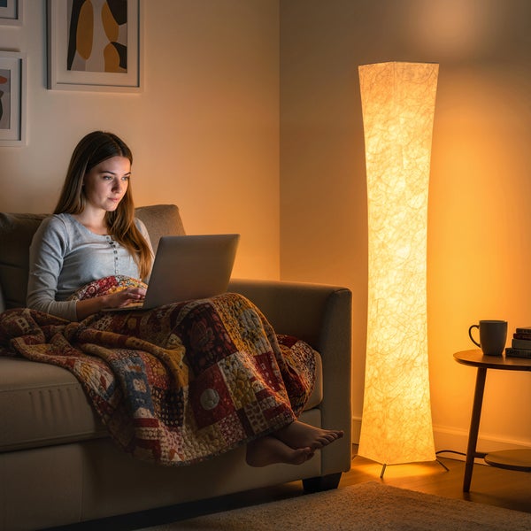 Frau sitzt mit Laptop auf Sofa neben Stehlampe