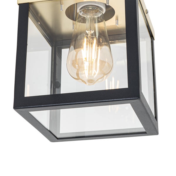 Deckenleuchte in Kastenform aus schwarzem Metall und Glas mit goldfarbener Montageplatte und sichtbarem Filament-Leuchtmittel.