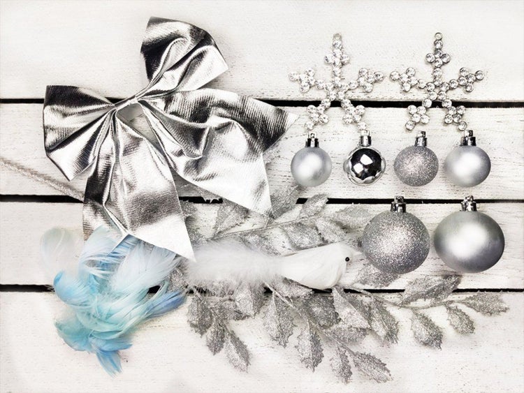Weihnachtsdekoration bestehend aus Schleife, Christbaumkugeln, Schneeflockenanhängern, Kunstzweigen und einer Vogel-Figur auf Holzuntergrund.