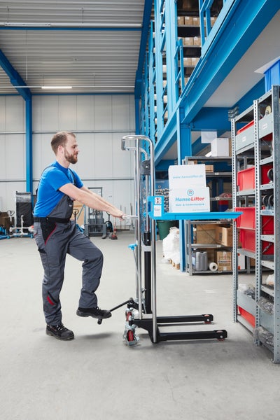 Ein Mann bedient einen manuellen Hochhubwagen von HanseLifter in einem Lager, um Kartons auf eine Ablagefläche zu heben.