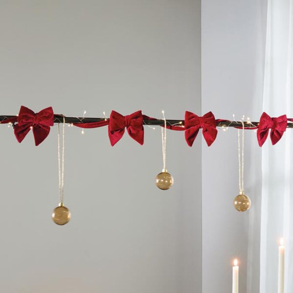 Weihnachtsdekoration Girlande mit Samtschleifen und hängenden Weihnachtskugeln inklusive Lichterkette für festliche Raumdekoration.