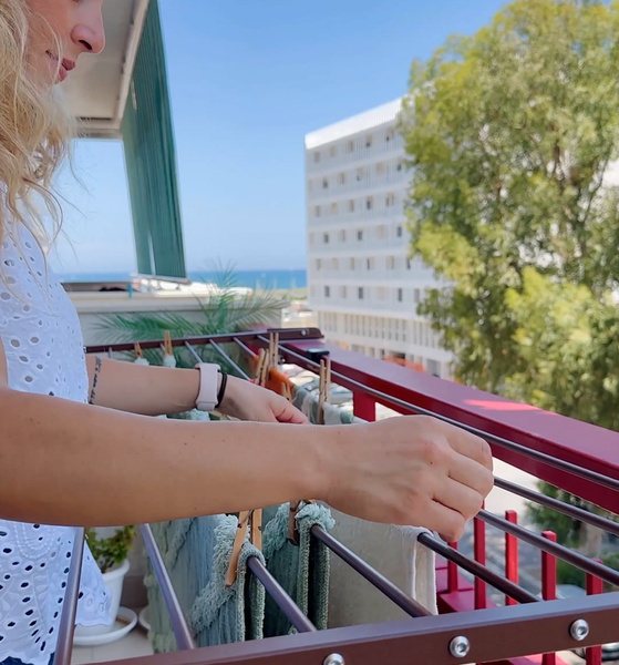 Frau hängt Wäsche auf einem Wäscheständer auf einem Balkon