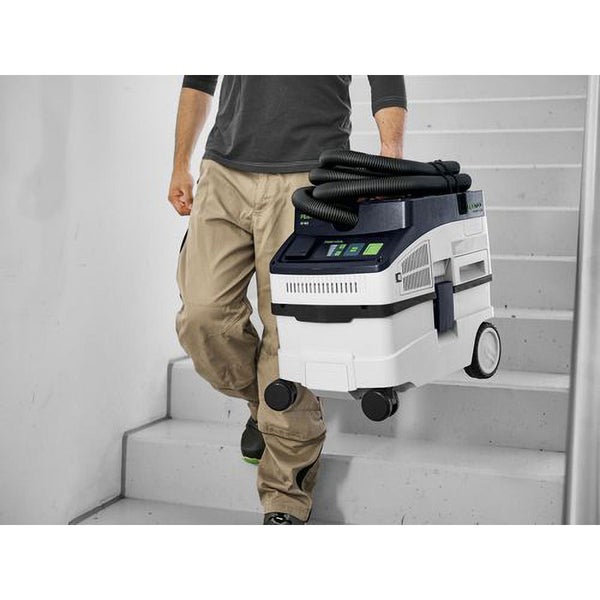 Eine Person trägt ein kompaktes Festool Absaugmobil an einem Handgriff eine Treppe hinauf.