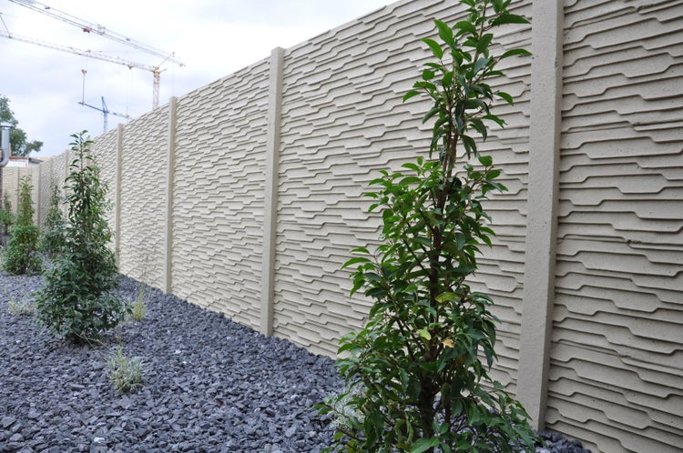 Betonzaun mit Zierpflanzen und Kies im Garten