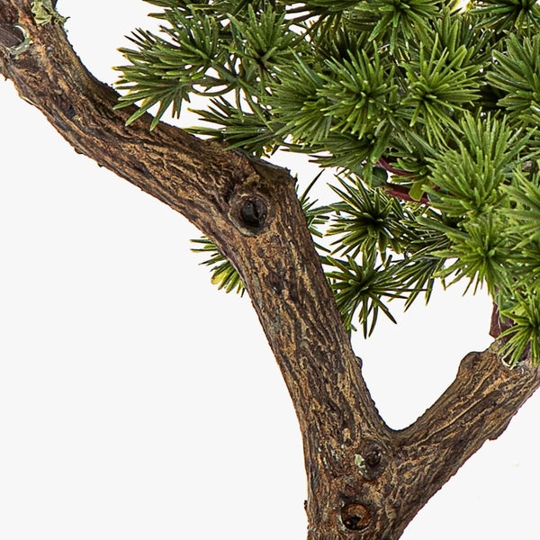 Detailansicht eines künstlichen Bonsai-Zweigs mit strukturierter Rinde und grünen Nadeln.