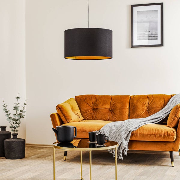 Modernes Wohnzimmer mit einer schwarz-goldenen Pendelleuchte über einem senfgelben Samtsofa und einem goldenen Couchtisch mit schwarzem Teeservice.