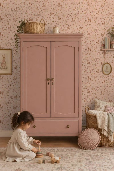Ein Kinderzimmer mit einem zweitürigen Schrank, einer Waldtapete mit Rehen und einem Mädchen, das auf dem Boden mit Holzspielzeug spielt.