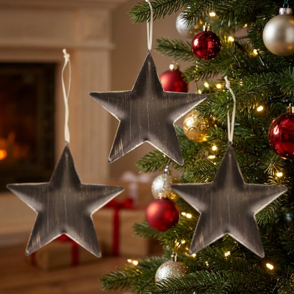Drei hängende Weihnachtssterne aus Metall mit antiker Optik als Dekoration für den Weihnachtsbaum vor einem Kamin.