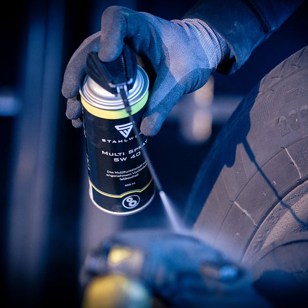 Eine Person mit Handschuhen hält eine Sprühdose Stahlwerk Multi Spray SW 40 vor einem Reifen.