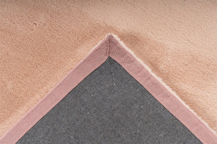 Nahaufnahme einer Teppichecke in Beige mit weicher, plüschiger Oberseite und grauer, gewebter Rückseite mit Textileinfassung.