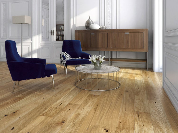 Helles Wohnzimmer mit Parkett aus Eiche, zwei blauen Sesseln, rundem Couchtisch und einem Sideboard aus Holz.