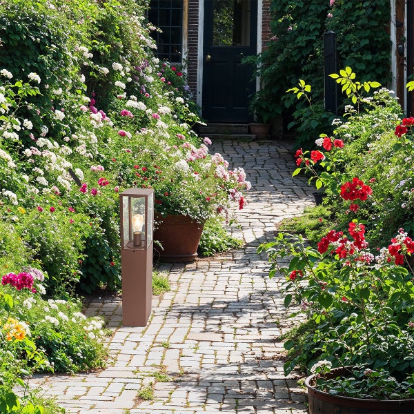 Moderne Wegeleuchte aus Metall auf einem gepflasterten Gartenweg inmitten von blühenden Blumen und Pflanzen.