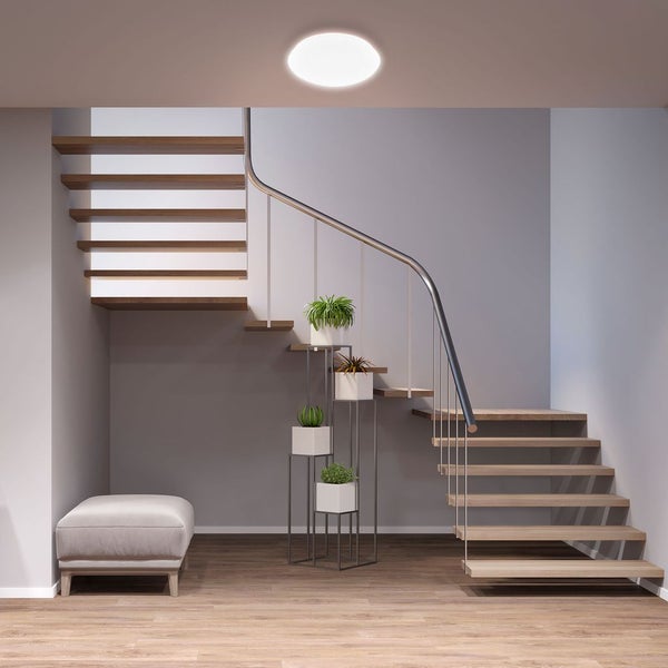 Runde LED-Deckenleuchte in einem modern eingerichteten Flur mit Holztreppe, Pflanzenständer und hellem Fußboden.