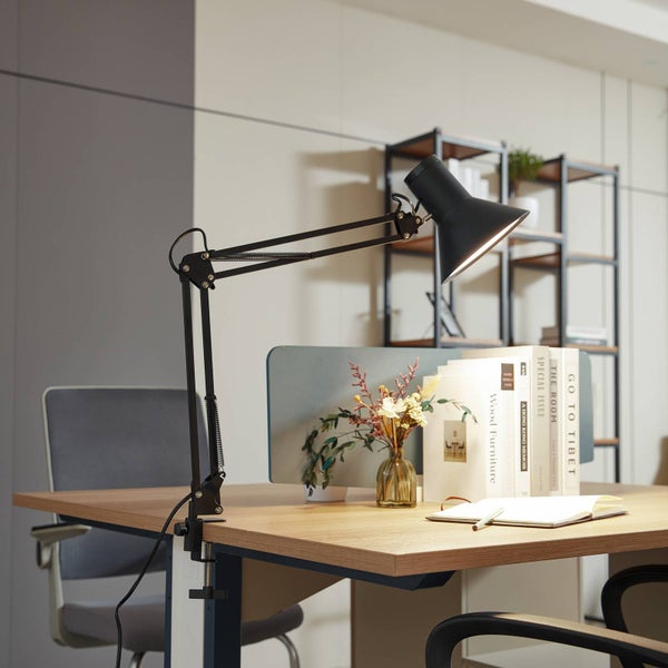 Schwarze, verstellbare Schreibtischleuchte mit Klemmbefestigung an einem Holztisch in einem hellen, organisierten Büro mit Büchern.