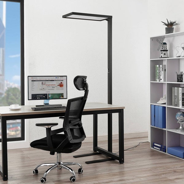 Helle Büroszene mit schwarzer LED-Stehleuchte über einem Schreibtisch mit Monitor, ergonomischem Bürostuhl und einem weißen Regal.