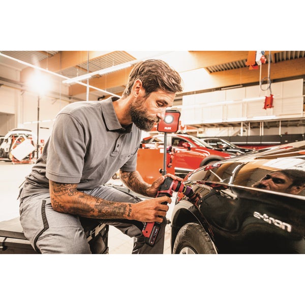 Ein Handwerker poliert mit einer kabellosen Poliermaschine die Karosserie eines Autos in einer hellen, professionellen Werkstatt.