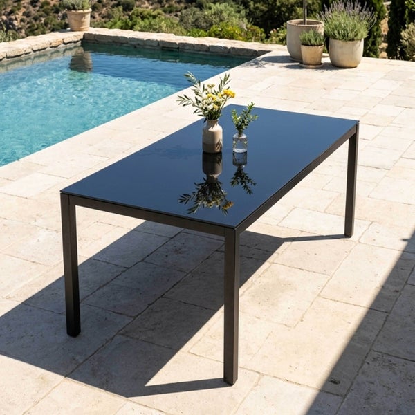 Moderner rechteckiger Gartentisch mit dunkler Glasplatte und Metallgestell auf einer Terrasse neben einem Pool.