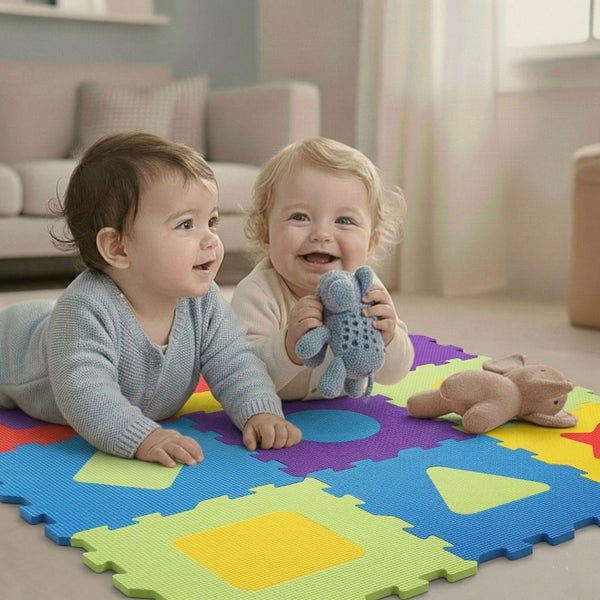 Zwei Babys spielen auf einer bunten Schaumstoff-Puzzlematte mit geometrischen Formen in einem hellen Wohnzimmer.