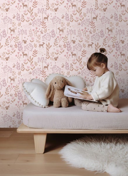 Mädchen liest ein Buch auf einem Bett vor einer Tapete mit Waldmotiven.