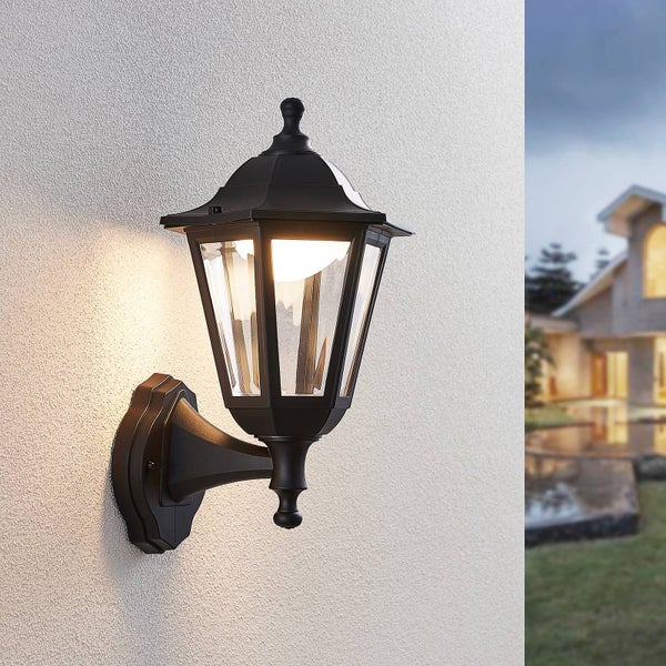 Klassische schwarze Außenwandleuchte in Laternenform mit Glaseinsätzen, montiert an einer Fassade und leuchtend.