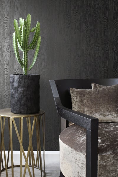 Dekoratives Zimmer mit Kaktus, Beistelltisch und Sessel vor einer dunklen Wand mit Holzmaserung