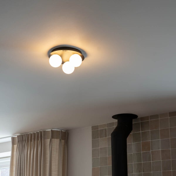 Moderne Deckenleuchte mit drei weißen Glaskugeln montiert an der Decke in einem Raum mit Fliesenwand und Vorhängen.