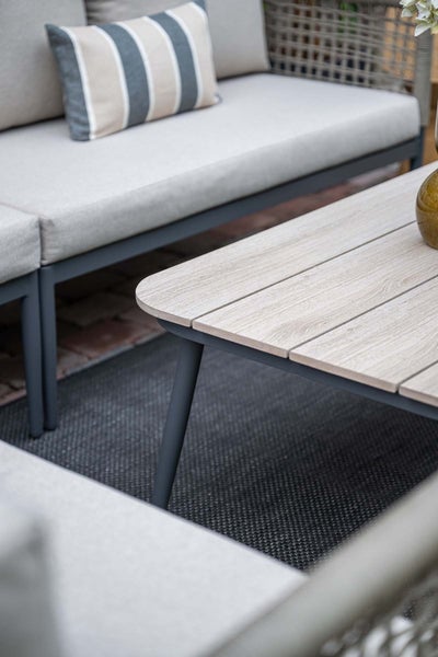 Moderne Garten-Lounge-Gruppe mit Sofa inklusive Polstern und einem Couchtisch mit Tischplatte in Holzoptik auf einem Outdoor-Teppich.
