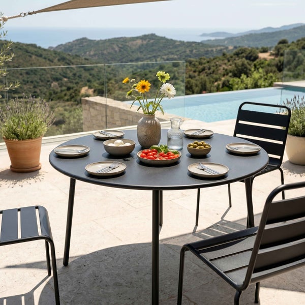 Moderne Garten-Essgruppe mit rundem schwarzem Metalltisch und Stühlen auf einer hellen Steinterrasse mit Pool und Bergblick.
