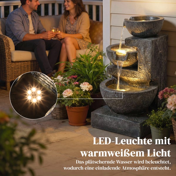 Mehrstufiger Gartenbrunnen in Steinoptik mit warmweißer LED-Beleuchtung auf einer Terrasse mit einem Paar im Hintergrund und Detailansicht der Lampen.