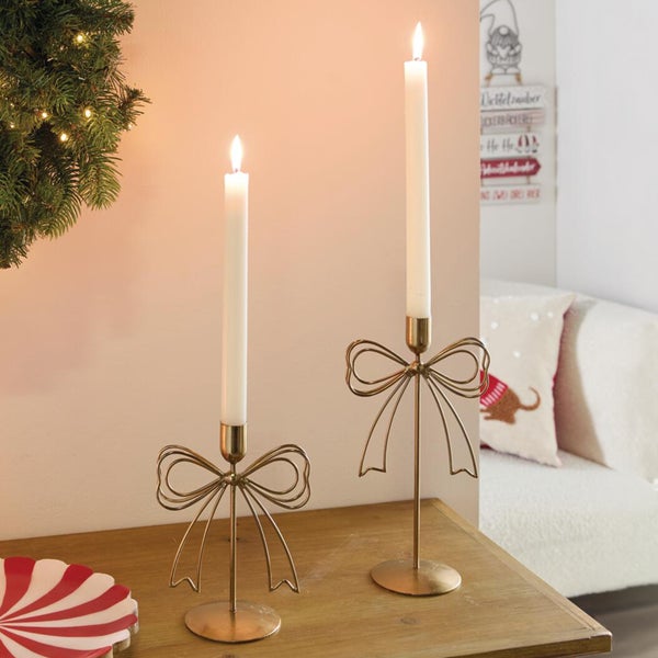 Zwei dekorative Kerzenständer aus Metall mit Schleifen Design und brennenden Stabkerzen auf einem Holztisch als weihnachtliche Dekoration.