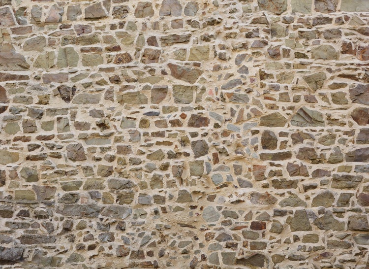 Nahaufnahme einer rustikalen Natursteinwand mit unregelmäßigen Steinen und sichtbaren Mörtelfugen für Wandverkleidung und Dekoration.