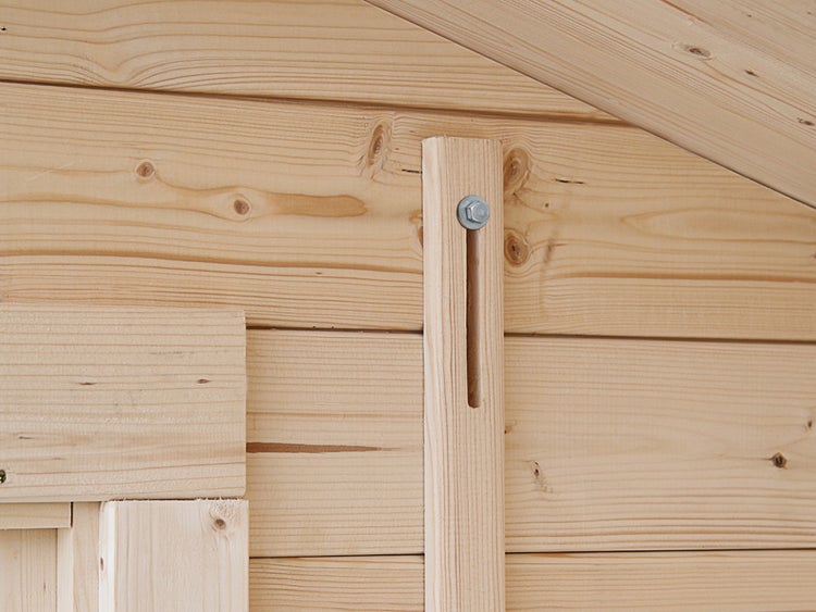 Sturmsicherung an einer Blockbohlenwand eines Gartenhauses aus Holz mit Sechskantschraube und Unterlegscheibe.