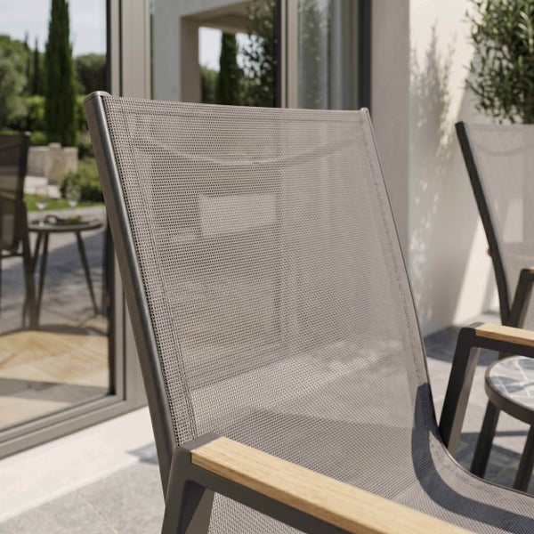 Nahaufnahme eines Gartenstuhls mit Netzgewebe, Aluminiumgestell und Armlehnen aus Holz auf einer Terrasse.