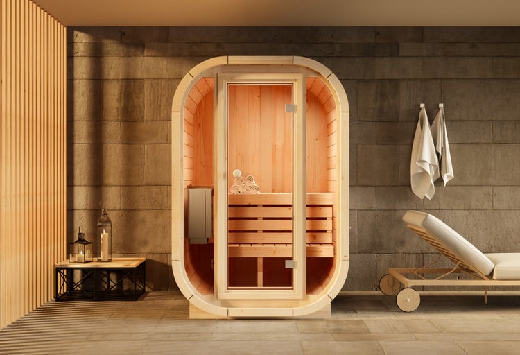 Moderne ovale Sauna aus Holz mit Glastür in einem hellen Wellnessbereich mit Steinwand und Liegestuhl.