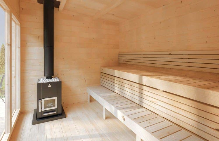 Innenansicht einer Holzsauna mit schwarzem Holzofen und mehrstufigen Holzbänken. Helles, geräumiges Design mit großen Fenstern.