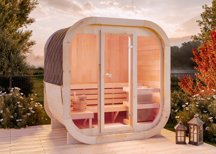 Moderne Außensauna aus hellem Holz mit Glasfront und abgerundeten Ecken auf einer Holzterrasse im Garten bei Sonnenuntergang.
